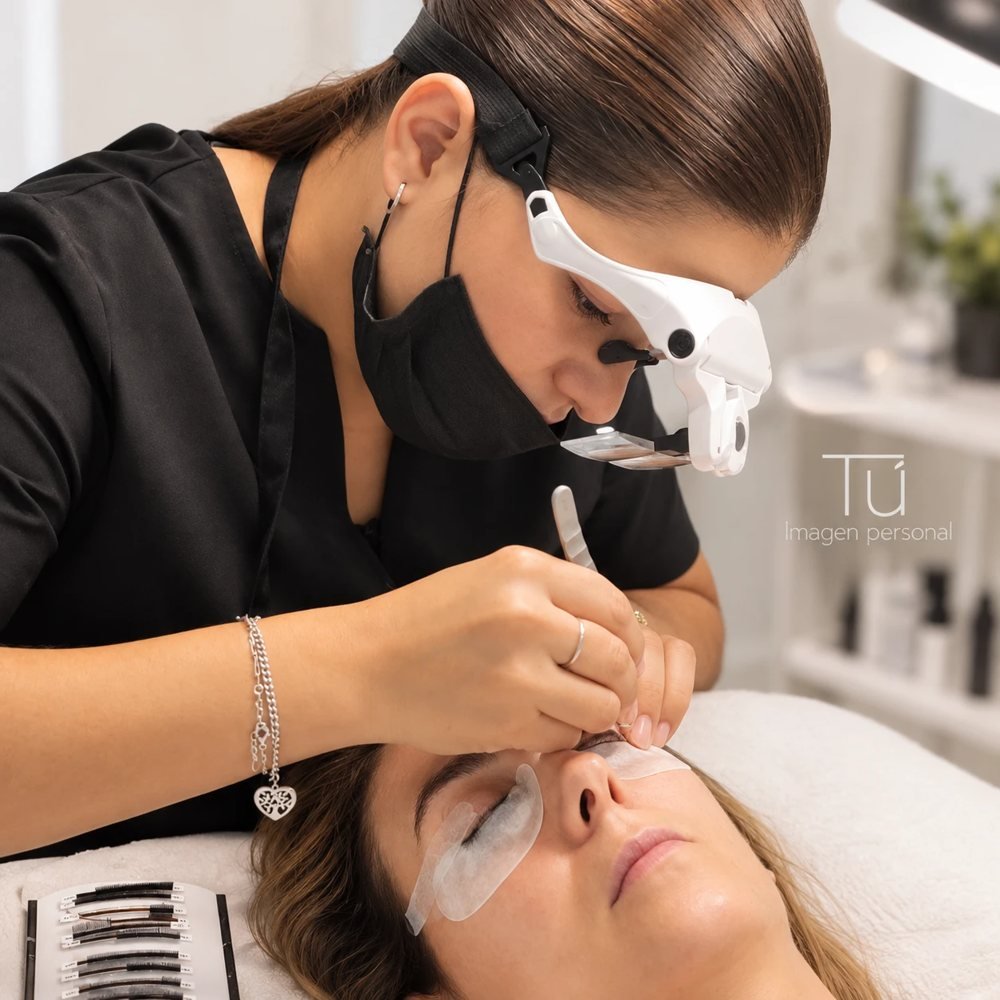 Profesional aplicando extensiones de pestañas con lupa en TÚ Imagen Personal